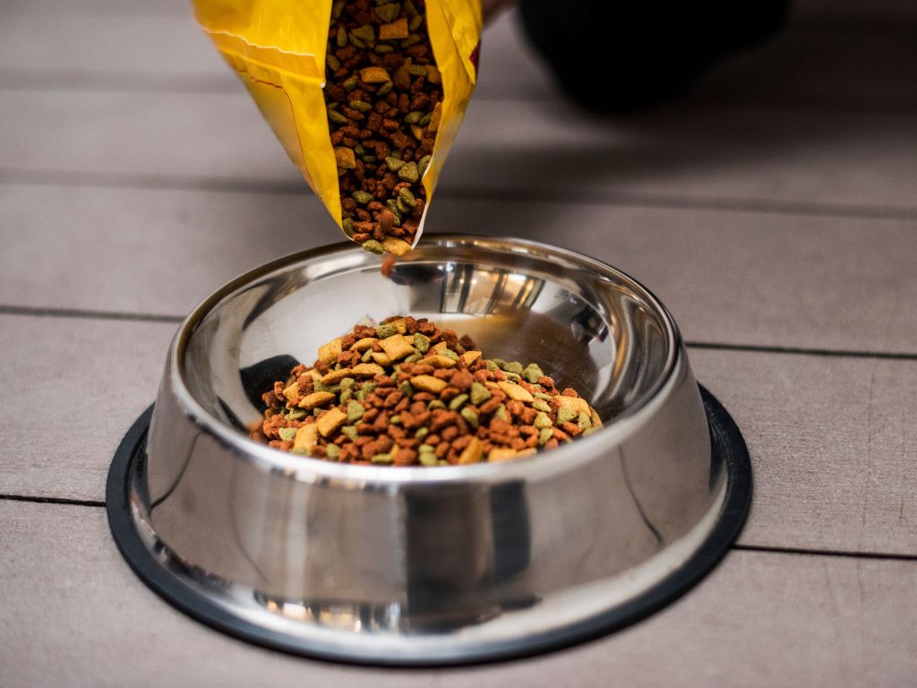 Dry pet food being poured from a yellow bag into a stainless steel bowl